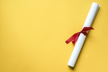 Zusammengerolltes Bachelorzeugnis vor gelbem Hintergrund